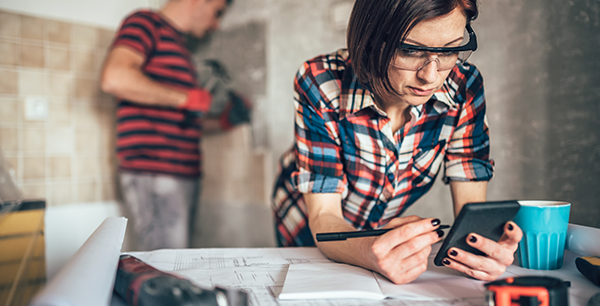 A female checking phone while husband drilling in the back ground